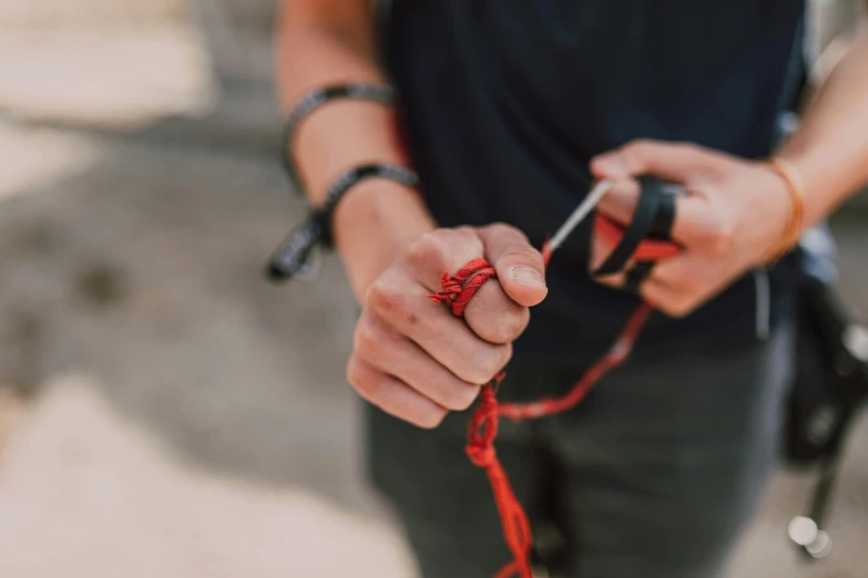 a close up of a person holding a pair of scissors, by Emma Andijewska, pexels contest winner, red wires wrap around, adventuring gear, 🕹️ 😎 🔫 🤖 🚬, rope