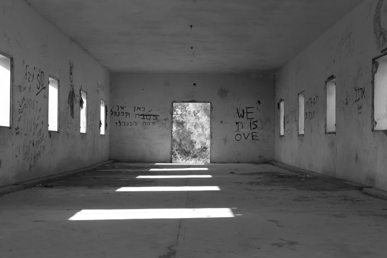 an empty room with graffiti on the walls, a black and white photo, by Jan Rustem, sun shafts, gray concrete, empty floor, abandoned in a desert