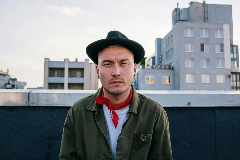 a man standing on top of a roof next to a tall building, a portrait, unsplash, graffiti, he‘s wearing a red neckerchief, frank dillane, philip selway (drums), portrait image