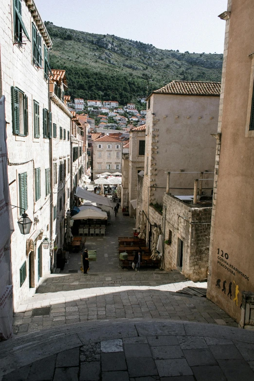 a narrow cobblestone street with tables and umbrellas, inspired by Ivan Lacković Croata, renaissance, walking down a marble stairwell, humongous view, from of thrones, long winding stairs going down