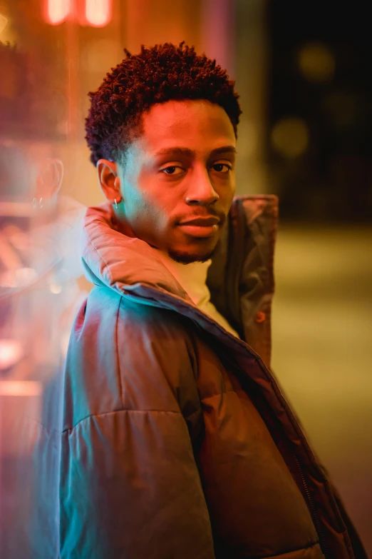 a man standing on a city street at night, an album cover, by Cosmo Alexander, pexels contest winner, model wears a puffer jacket, mkbhd, headshot portrait, hero pose colorful city lighting