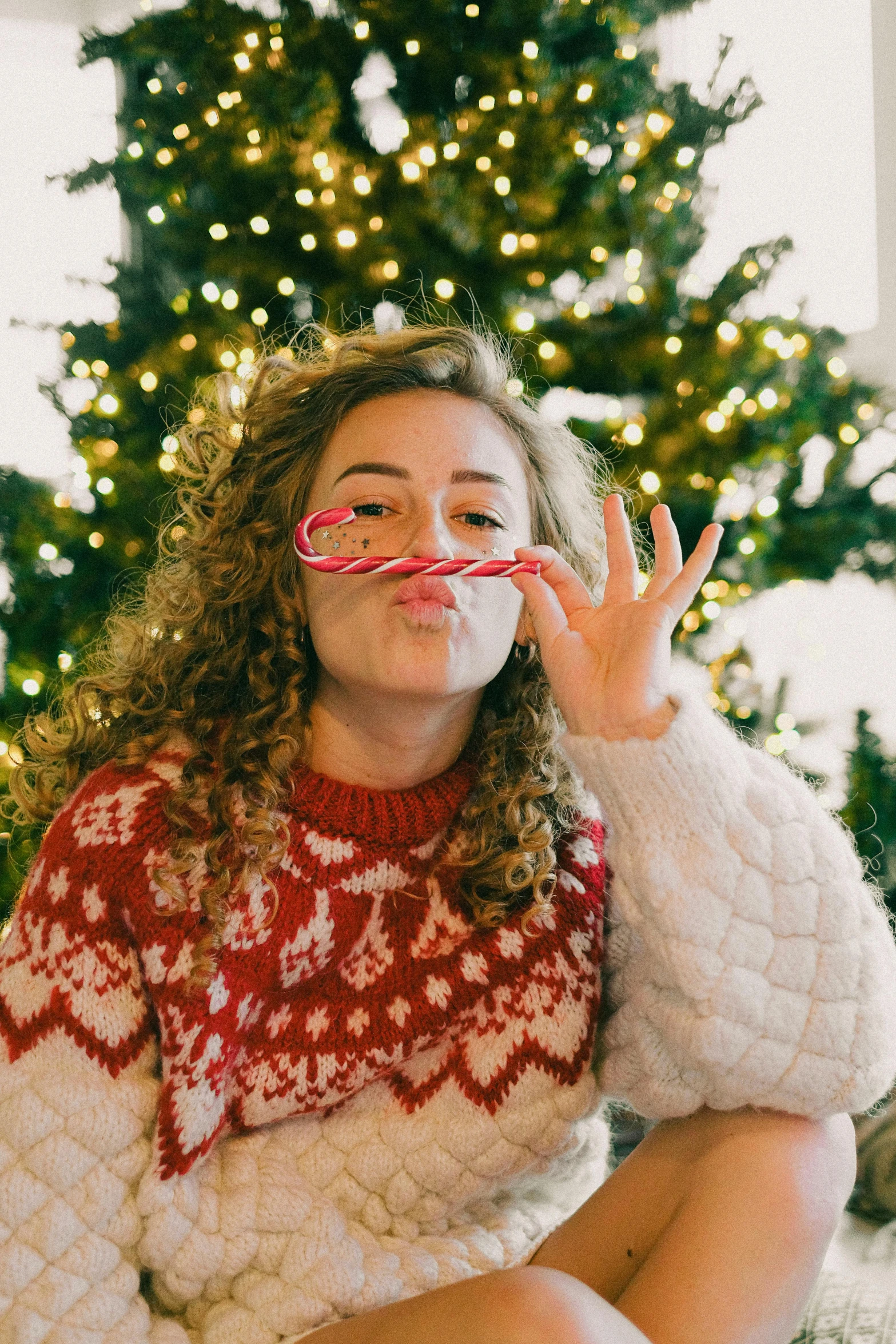 a woman blowing soap on her face in front of a christmas tree, by Carey Morris, pexels, with long curly, candy canes, gif, college