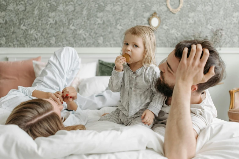 a man laying on top of a bed next to a little girl, by Adam Marczyński, pexels contest winner, having a snack, husband wife and son, gif, a group of people