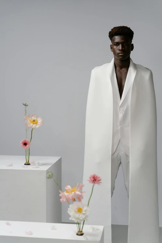 a man standing next to three vases with flowers in them, an album cover, inspired by Emanuel de Witte, neo-figurative, wearing futuristic white suit, wearing a luxurious silk cloak, showstudio, adut akech