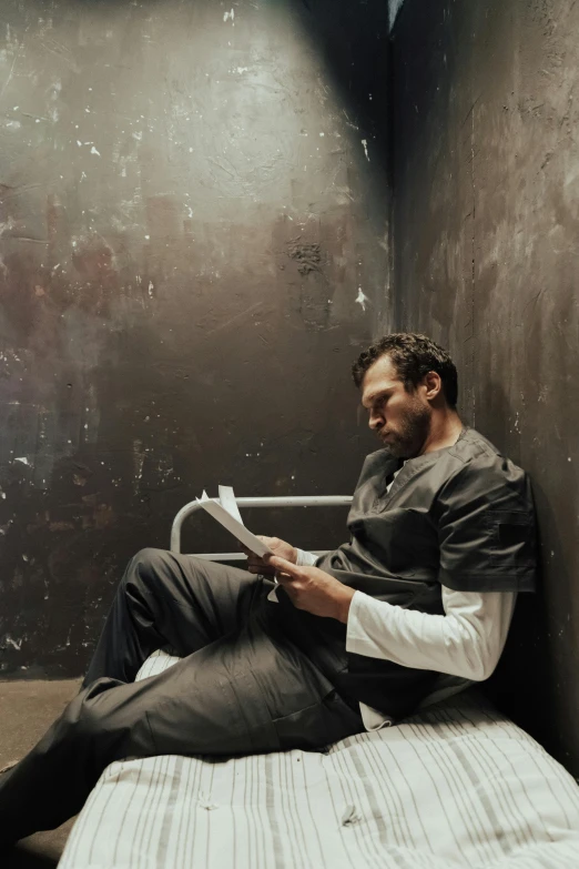 a man sitting on a bed reading a book, inspired by Joseph Morgan Henninger, pexels contest winner, serial art, in a prison cell, herry cavill, ( ( theatrical ) ), criminal mugshot