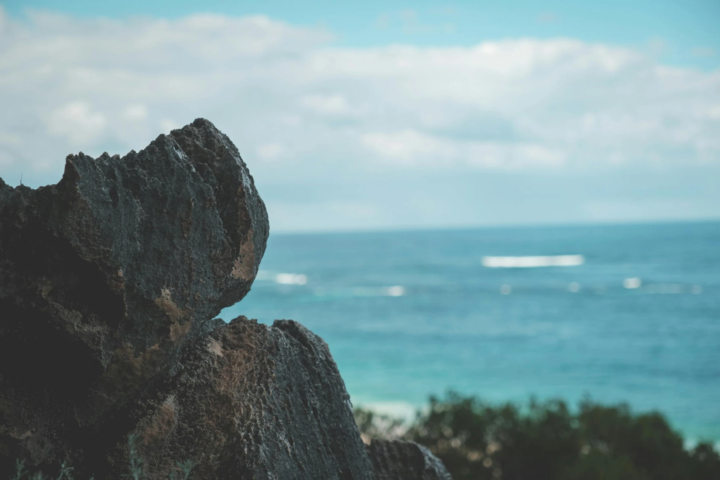 a close up of a rock with the ocean in the background, unsplash, manly, view from a distance, staring at you, blue