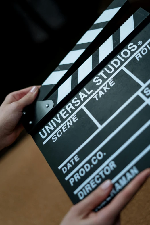 a person holding a clap board in their hands, a picture, shutterstock, unreal engine. film still, mgm studios, universe, movie set”