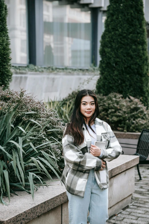 a woman standing on a sidewalk in front of a building, inspired by helen huang, pexels contest winner, wearing a flannel shirt, sitting on a park bench, vancouver, wearing a fancy jacket