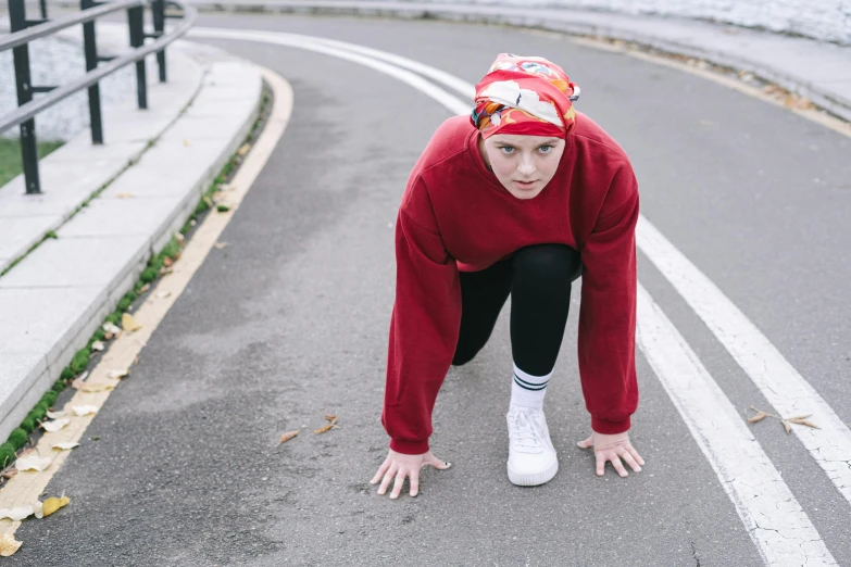 a woman standing on her knees on the side of a road, inspired by Louisa Matthíasdóttir, pexels contest winner, red sweatband, wearing a track suit, non binary model, people running