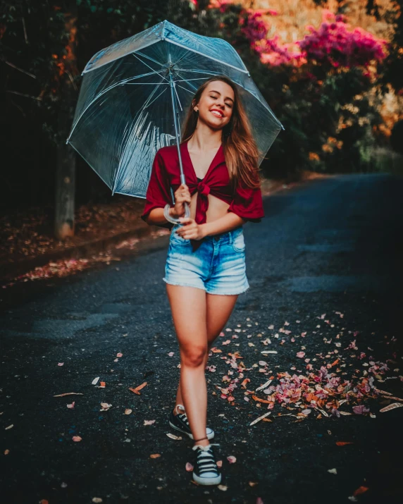 a woman walking down a road holding an umbrella, by Robbie Trevino, satisfied pose, wearing shorts, in a park, brooke ashling