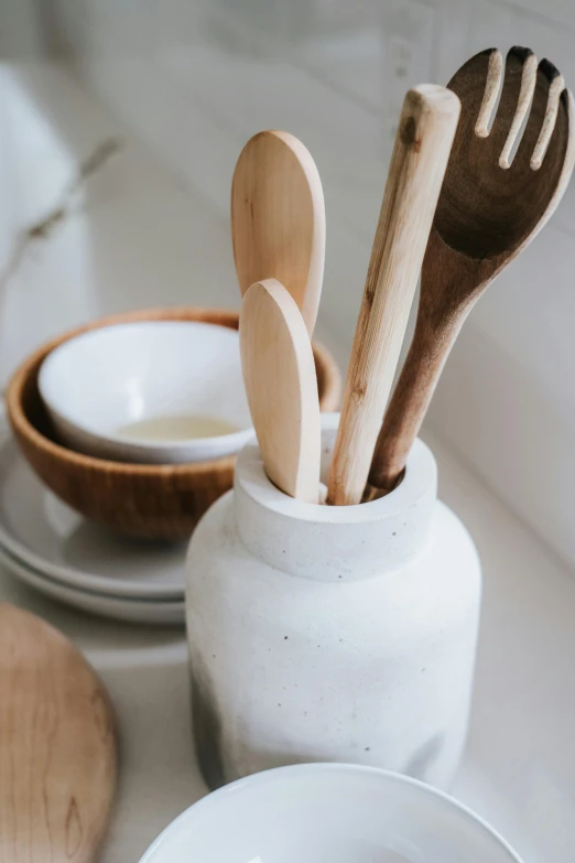 a table topped with bowls and wooden utensils, a still life, unsplash, bottle, white, close - up photograph, kitchen