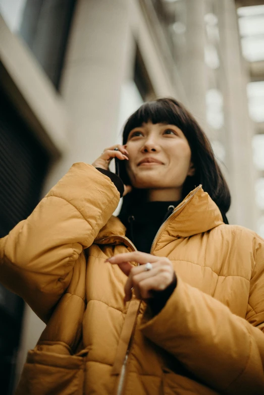 a woman in a yellow jacket talking on a cell phone, trending on pexels, ethnicity : japanese, brown, supportive, screensaver