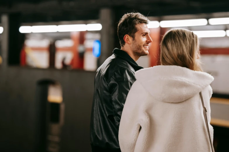 a man and a woman standing in front of a train, trending on pexels, underground facility, flirting smiling, wearing leather coat, central station in sydney