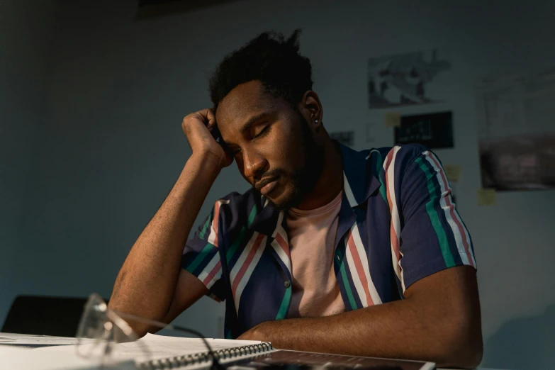 a man sitting at a desk with his head in his hands, pexels contest winner, academic art, dark skinned, looking tired, avatar image, studyng in bedroom