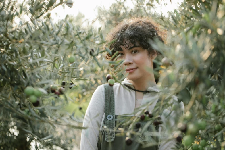 a woman in overalls standing among olive trees, pexels, renaissance, dark short curly hair smiling, charli bowater and artgeem, egor letov, [ organic