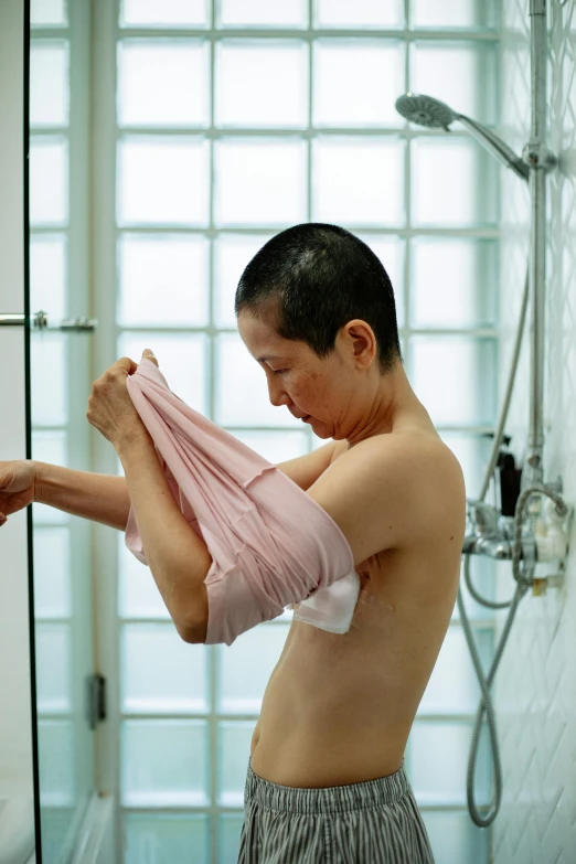 a man standing in front of a shower holding a towel, shin hanga, partially cupping her hands, covered in pink flesh, older woman, wet tshirt