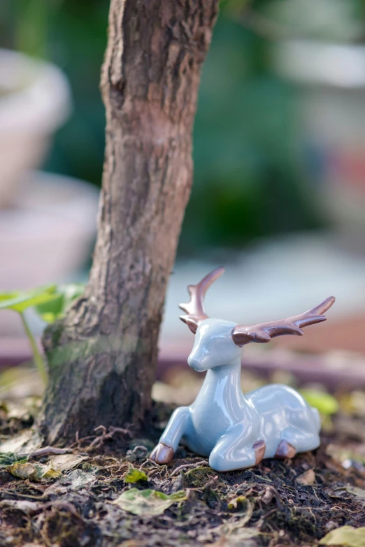 a figurine of a deer sitting next to a tree, pastel blue, natural mini gardens, shiny crisp finish, poseidon