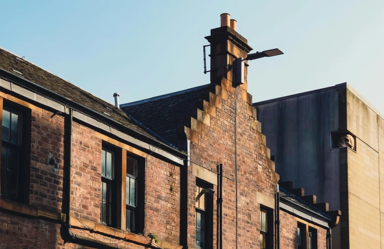 a tall brick building with a clock on top of it, by Andrew Allan, pexels contest winner, arts and crafts movement, glasgow, simple gable roofs, hard morning light, looking around a corner