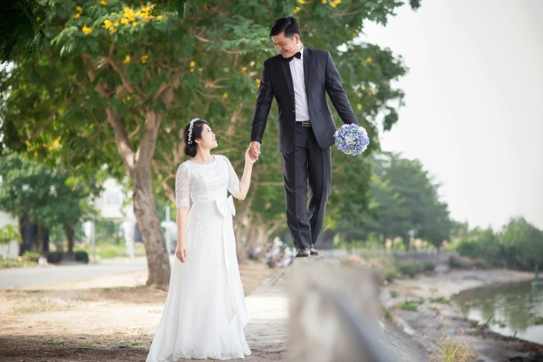 a man in a tuxedo and a woman in a wedding dress holding hands, inspired by Cui Bai, happening, near a jetty, jumping, in style of lam manh, with a tree in the background
