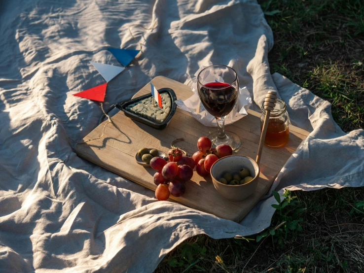 a wooden cutting board sitting on top of a grass covered field, a still life, by Niko Henrichon, pexels contest winner, figuration libre, red wine, with square glasses, raf grassetti, red flags holiday