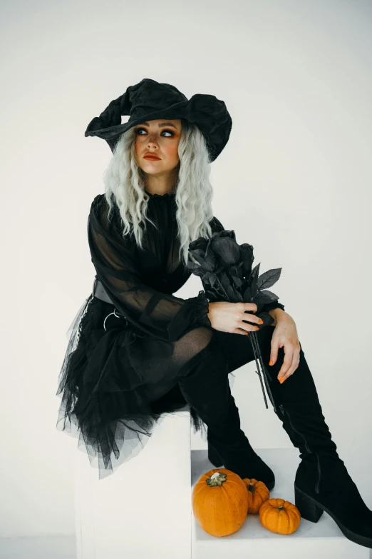 a woman in a witch costume sitting on a block, pexels contest winner, modeling photograph kerli koiv, black hat, on a gray background, witchcore clothes