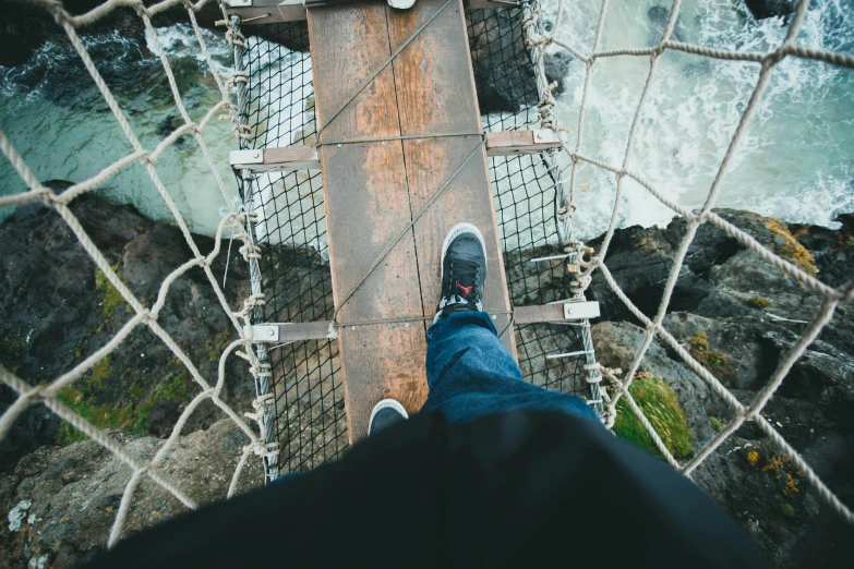 a person standing on a rope bridge over a body of water, pexels contest winner, looking down from above, wearing jeans, 🦩🪐🐞👩🏻🦳, sneaker