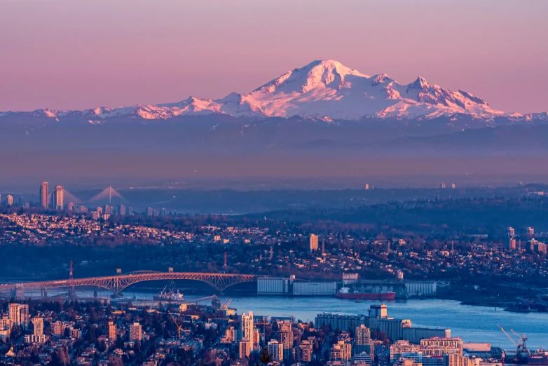 a view of a city with a mountain in the background, by Meredith Dillman, pexels contest winner, cascadia, pink golden hour, with a snowy mountain and ice, panoramic