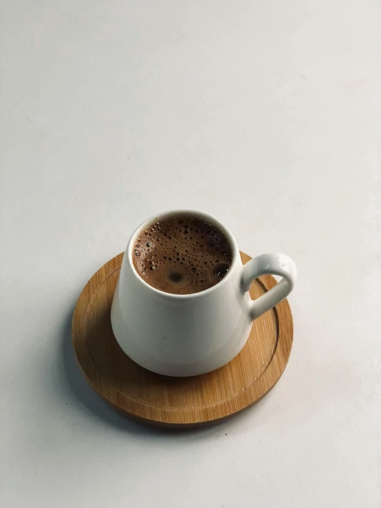 a cup of coffee sitting on top of a wooden coaster, hurufiyya, profile image, hot cocoa drink, close - up photograph, jakarta