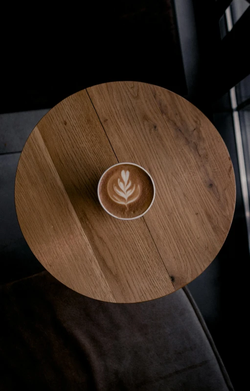 a cup of coffee sitting on top of a wooden table, by Robbie Trevino, round design, multiple stories, uk, nightcap