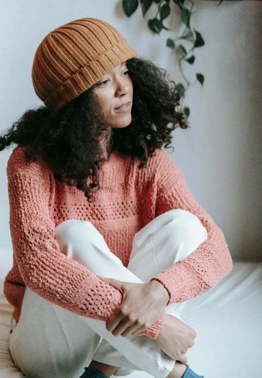 a woman sitting on top of a bed wearing a hat, trending on pexels, wearing casual sweater, coral, highly textured, sustainable materials