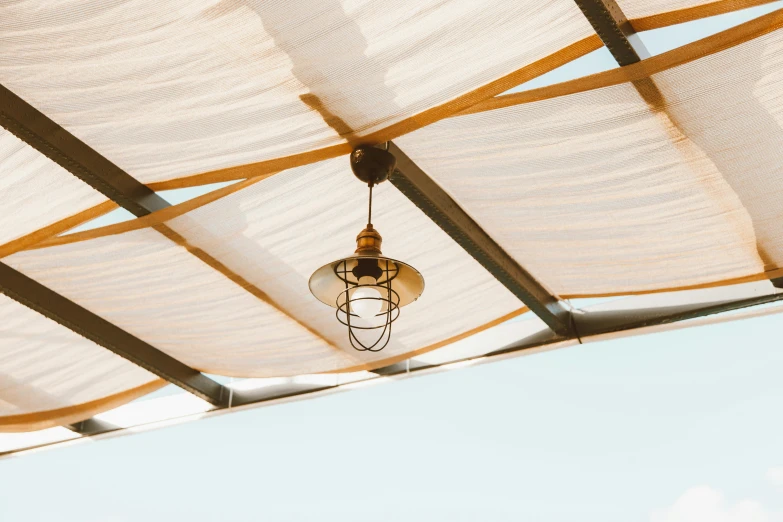 a light hanging from the ceiling of a covered area, inspired by Christo, trending on pexels, light and space, rooftop romantic, ivory and copper, well shaded, bright sky