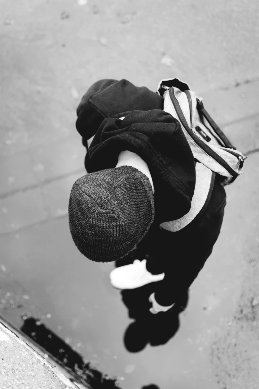 a black and white photo of a person on a skateboard, inspired by Louis Stettner, with a backpack, wearing beanie, from above, hugging