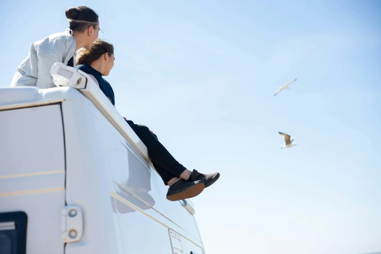 a man and a woman sitting on top of a boat, pexels contest winner, arabesque, next to an rv, birds in the sky, close up shot from the side, leg high