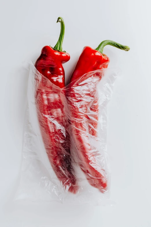 two red peppers wrapped in plastic on a white surface, inspired by Géza Dósa, unsplash, mexico, detailed product image, hanging, long chin