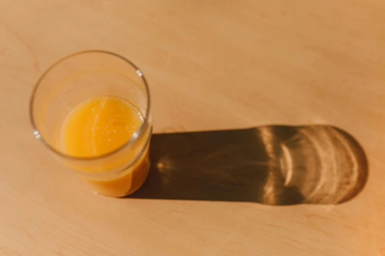 a glass of orange juice sitting on top of a wooden table, unsplash, sun puddle, rinko kawauchi, without text, josh grover