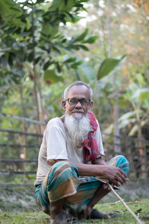 a man sitting on top of a lush green field, bengal school of art, very long silver beard, portrait image, bangladesh, seated on wooden chair