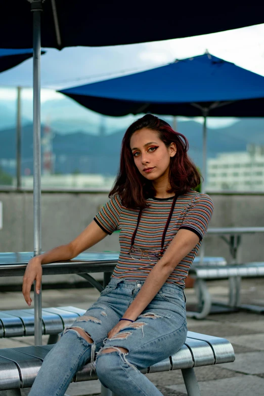 a woman sitting on a bench under an umbrella, a colorized photo, pexels contest winner, striped shirt, angela sarafyan, portrait of vanessa morgan, rooftop