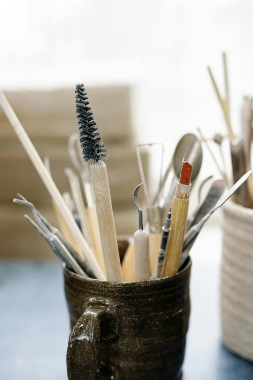 a cup filled with brushes sitting on top of a table, vases and bottles, blades, up-close, sustainable materials
