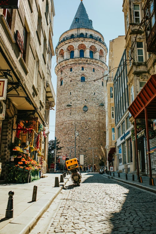 a narrow cobblestone street with a tall tower in the background, inspired by Altoon Sultan, pexels contest winner, art nouveau, one motorbike in center of frame, ottoman sultan, 2 5 6 x 2 5 6, city views