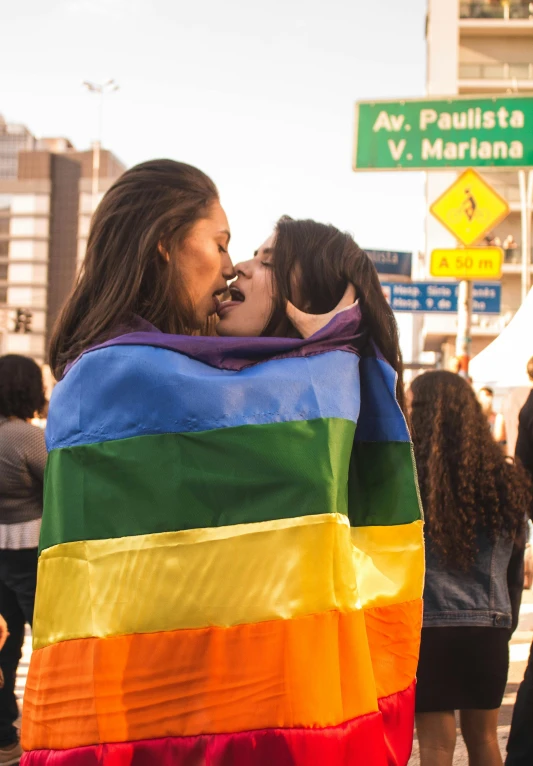a couple of women standing next to each other on a street, by Olivia Peguero, happening, lgbt flag, hugging, in sao paulo, 🚿🗝📝