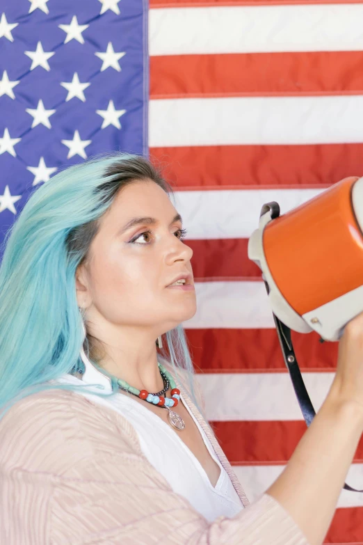 a woman with blue hair using a megaphone in front of an american flag, trending on reddit, american romanticism, orange and teal color, mug shot, native american, politics