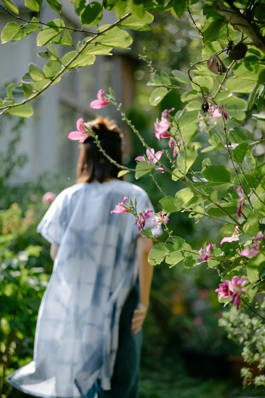 a woman walking through a lush green garden, a picture, happening, wearing a tie-dye t-shirt, vines and flowers, over the shoulder view, soft blue and pink tints