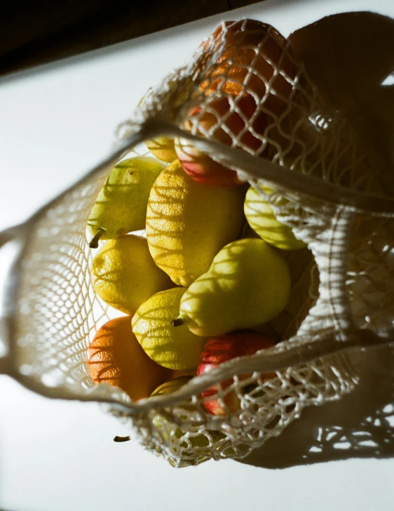 a mesh bag filled with apples and oranges, by Emanuel de Witte, unsplash, net art, back lit, pear, indoor shot, olives