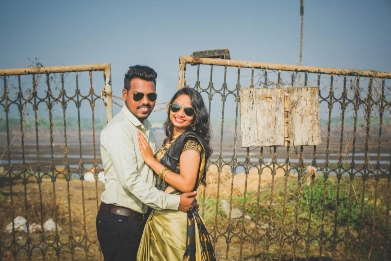 a man and woman standing in front of a fence, a picture, pexels contest winner, howrah bridge, sunny environment, happy couple, brown