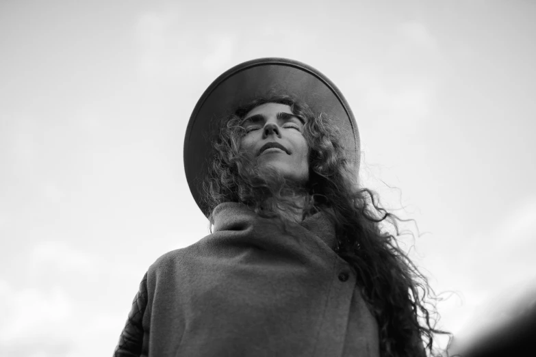 a black and white photo of a woman wearing a hat, unsplash, with long curly hair, wearing hay coat, sun behind him, halo over her head