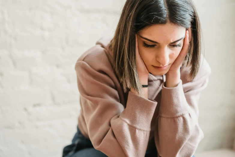 a woman sitting on a bed with her head in her hands, trending on pexels, wearing casual sweater, devastated, sitting on a mocha-colored table, realistic »