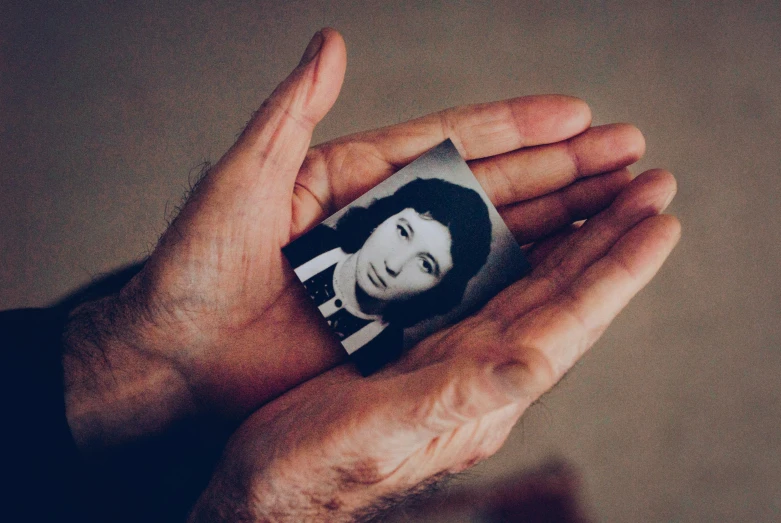 a hand holding a black and white photo of a woman, by Lucia Peka, pexels, a very sad man, 1980s photo, cardboard, portrait of small