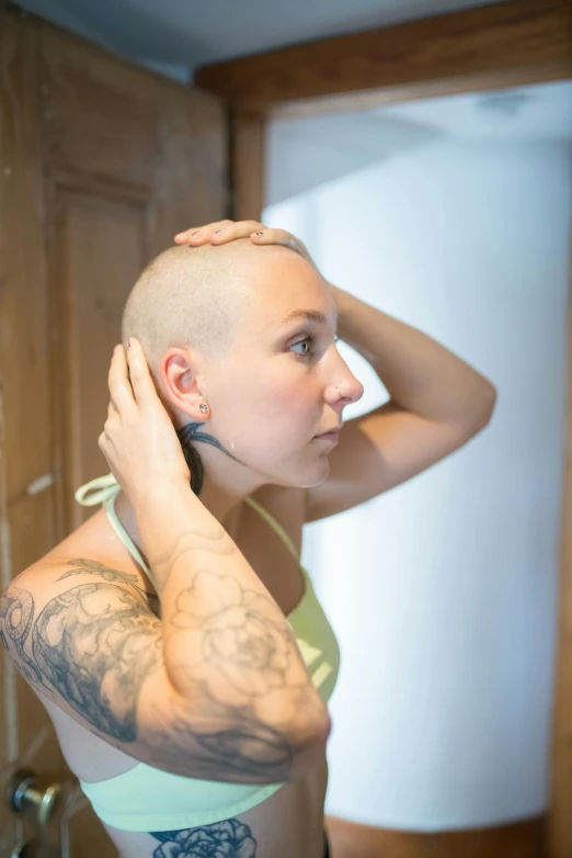 a woman with a shaved head standing in front of a mirror, a tattoo, unsplash, wearing a headset, shaven stubble, set photo