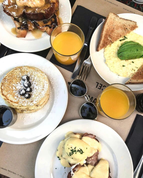 a table topped with plates of food and glasses of orange juice, a photo, by Robbie Trevino, trending on unsplash, pancakes, conde nast traveler photo, yellow and charcoal, 🎀 🍓 🧚
