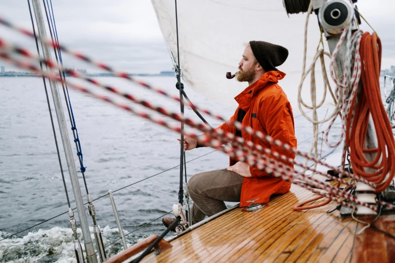 a man in an orange jacket sitting on a boat, pexels contest winner, he's on an old sailing boat, wind rose, owen klatte, food. craft and adventure